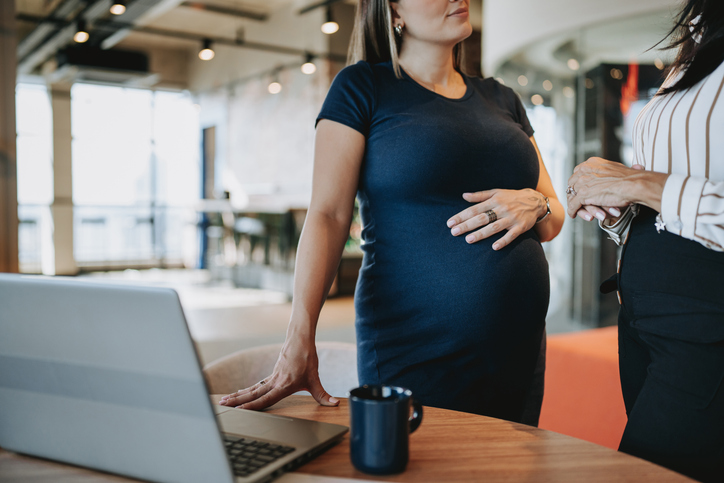 A pregnant women holding her stomach talking to another woman